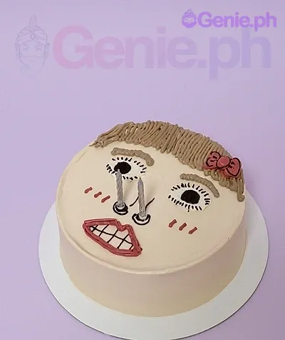 A white 1-tier cake themed around a hand-drawn girl's face, featuring two silver candles as eyes, piped brown hair, and a pink bow. A white 1-tier cake themed around a hand-drawn girl's face, featuring two silver candles as eyes, piped brown hair, and a pink bow.