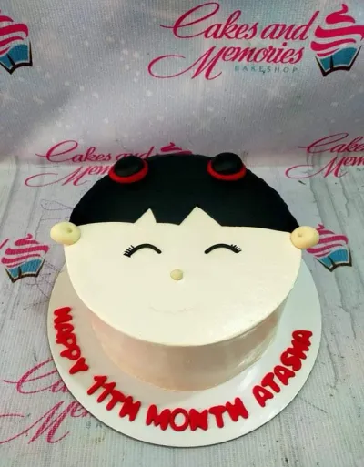 A white 1-tier round cake themed as a girl's face, featuring black fondant hair, red hair ties, facial features, and a message on the base board. A white 1-tier round cake themed as a girl's face, featuring black fondant hair, red hair ties, facial features, and a message on the base board.