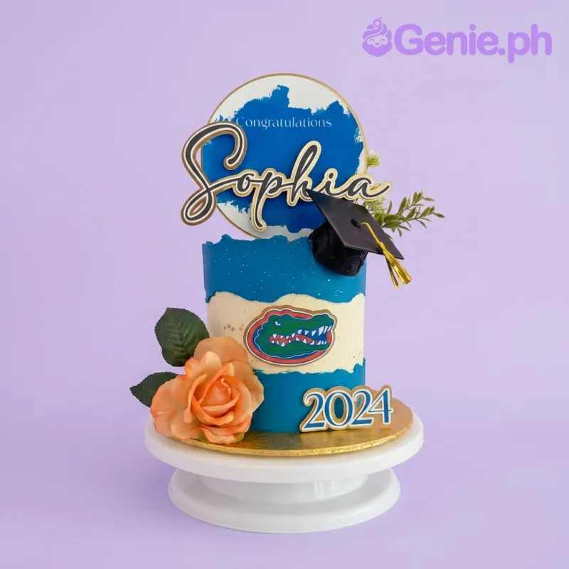 A blue and white 1 Tier Graduation cake, featuring Florida Gators logo, graduation cap, and orange rose. A blue and white 1 Tier Graduation cake, featuring Florida Gators logo, graduation cap, and orange rose.