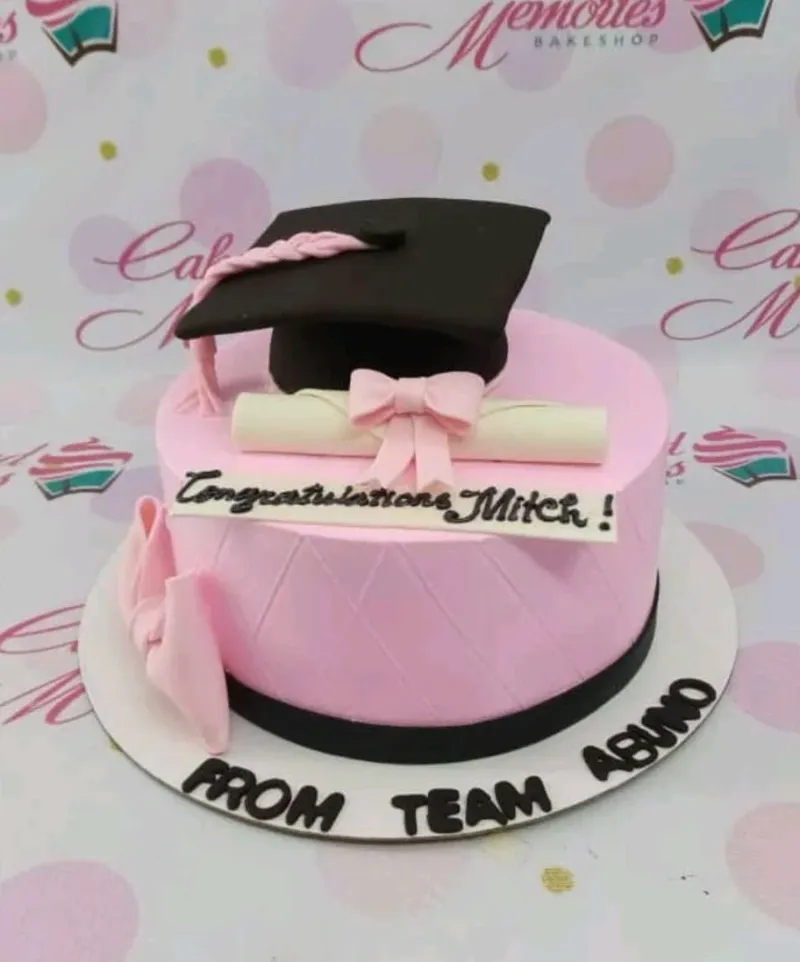 A pink 1 Tier Graduation cake with a black cap, a white diploma with pink bow, and a quilted icing pattern. A pink 1 Tier Graduation cake with a black cap, a white diploma with pink bow, and a quilted icing pattern.