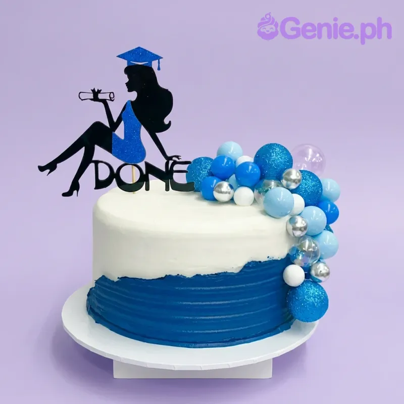 A white and navy blue 1-Tier Graduation cake, with a graduate silhouette topper and blue, white, silver decorative balls. A white and navy blue 1-Tier Graduation cake, with a graduate silhouette topper and blue, white, silver decorative balls.