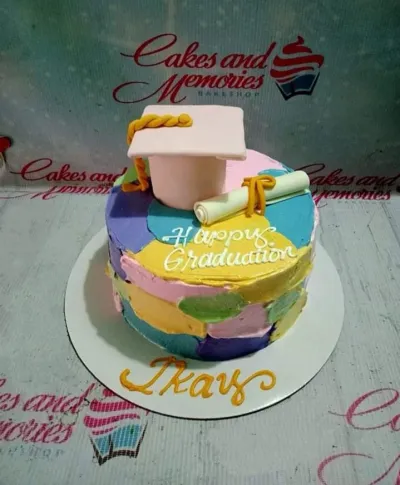 A white 1-tier cake with multicolored palette knife icing, themed Graduation, featuring a pink cap and white diploma. A white 1-tier cake with multicolored palette knife icing, themed Graduation, featuring a pink cap and white diploma.