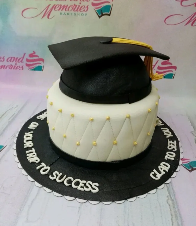 A white 1 Tier Fondant cake themed around Graduation, featuring a black graduation cap, yellow tassel, and quilted pattern with gold beads. A white 1 Tier Fondant cake themed around Graduation, featuring a black graduation cap, yellow tassel, and quilted pattern with gold beads.