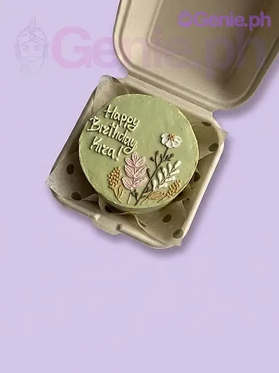 A light green bento cake themed around florals, featuring pink and white icing flowers and a white 'Happy Birthday Kira!' message. A light green bento cake themed around florals, featuring pink and white icing flowers and a white 'Happy Birthday Kira!' message.