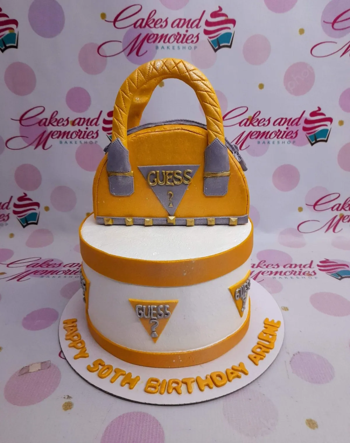 Yellow and white Guess brand themed birthday cake with a 3D fondant handbag topper and Guess logo triangles. Yellow and white Guess brand themed birthday cake with a 3D fondant handbag topper and Guess logo triangles.