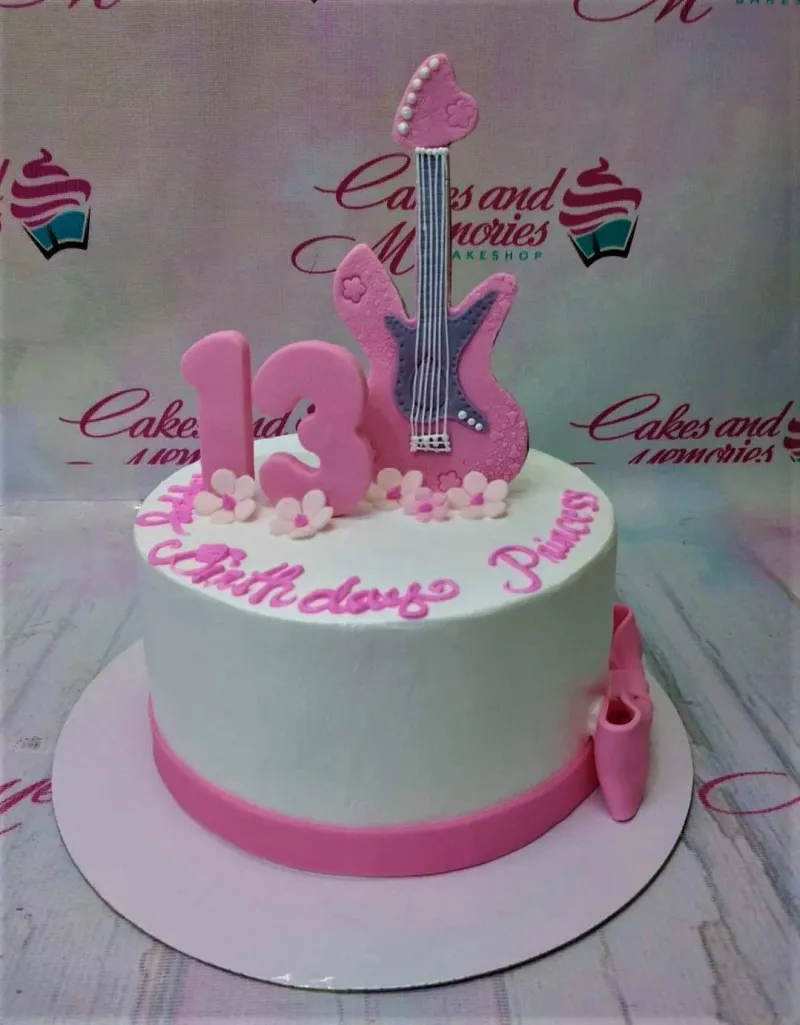 A white 1-tier cake with a pink fondant guitar, a pink number 13, and small pink flowers. A white 1-tier cake with a pink fondant guitar, a pink number 13, and small pink flowers.