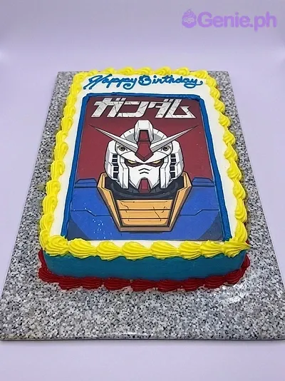 A blue and white rectangle Gundam cake, featuring a large Gundam character printout and yellow piped borders. A blue and white rectangle Gundam cake, featuring a large Gundam character printout and yellow piped borders.