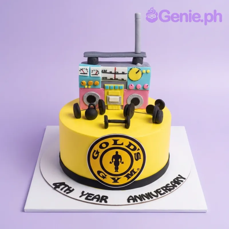 A yellow 1-tier fondant Gym Anniversary cake, featuring a boombox, dumbbells, kettlebell, and a Gold's Gym logo. A yellow 1-tier fondant Gym Anniversary cake, featuring a boombox, dumbbells, kettlebell, and a Gold's Gym logo.