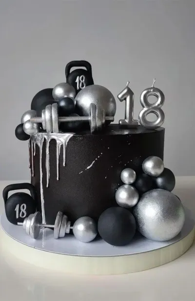 Black 18th birthday cake with silver drip, gym-themed kettlebell and dumbbell toppers, and silver number 18 candles. Black 18th birthday cake with silver drip, gym-themed kettlebell and dumbbell toppers, and silver number 18 candles.
