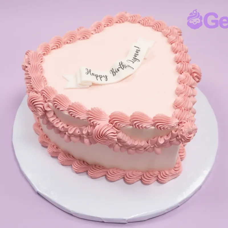 Pink heart-shaped birthday cake with a Happy Birthday banner and piped icing borders Pink heart-shaped birthday cake with a Happy Birthday banner and piped icing borders