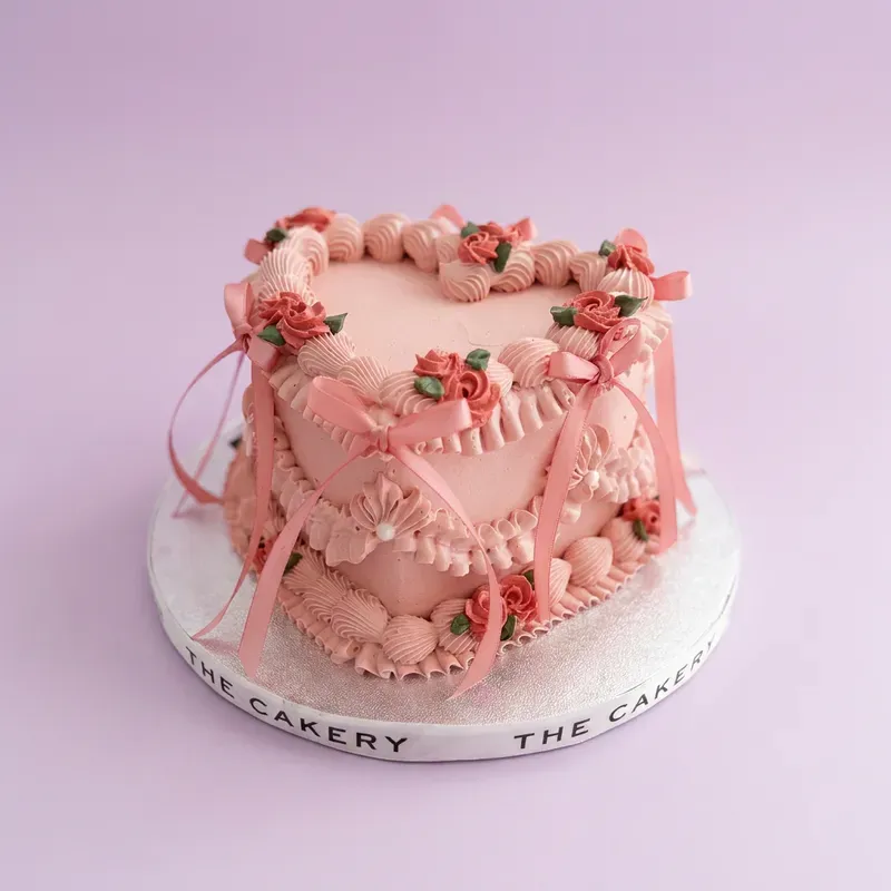 Heart Cake cake design — 1 layer soft icing cake in pink — with piped roses on top, and satin ribbons on sides Heart Cake cake design — 1 layer soft icing cake in pink — with piped roses on top, and satin ribbons on sides