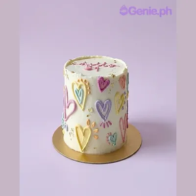 White single-tier cake with colorful piped icing hearts and gold leaf accents White single-tier cake with colorful piped icing hearts and gold leaf accents