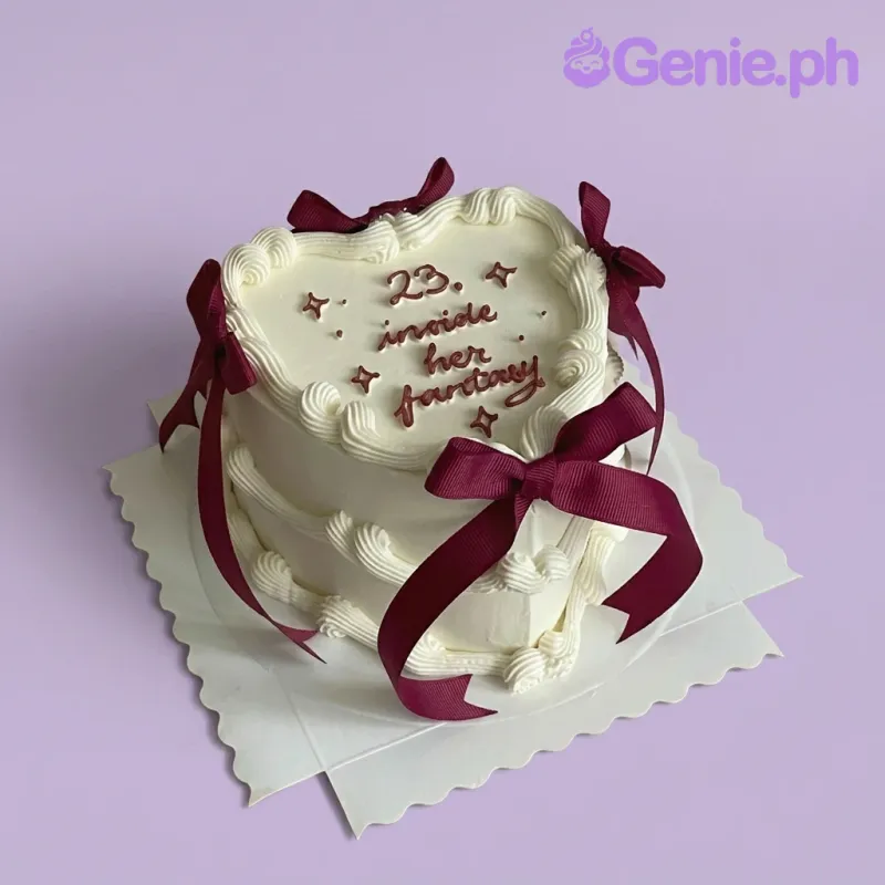White heart-shaped minimalist cake with dark red piped icing text and matching satin ribbons on a white scalloped base. White heart-shaped minimalist cake with dark red piped icing text and matching satin ribbons on a white scalloped base.