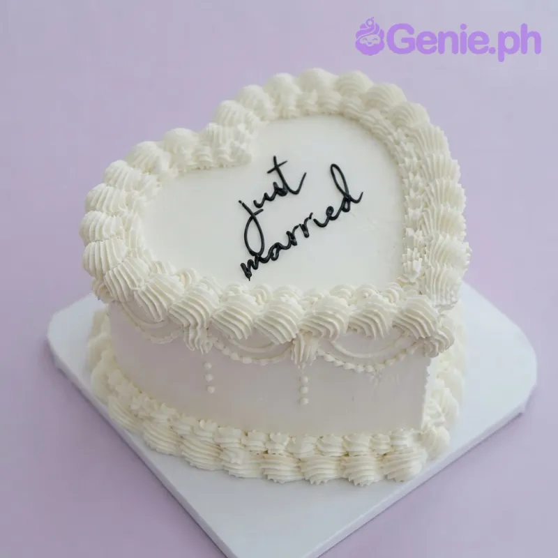 White heart-shaped cake with smooth soft icing, piped shell borders, and black piped script text White heart-shaped cake with smooth soft icing, piped shell borders, and black piped script text