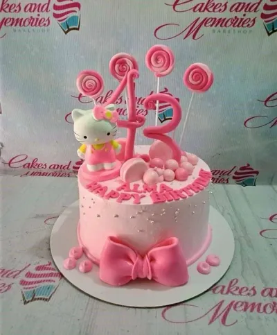 A pink 1-Tier cake themed around Hello Kitty, featuring a Hello Kitty figure, a large number 13 topper, pink swirl lollipops, and a pink bow. A pink 1-Tier cake themed around Hello Kitty, featuring a Hello Kitty figure, a large number 13 topper, pink swirl lollipops, and a pink bow.