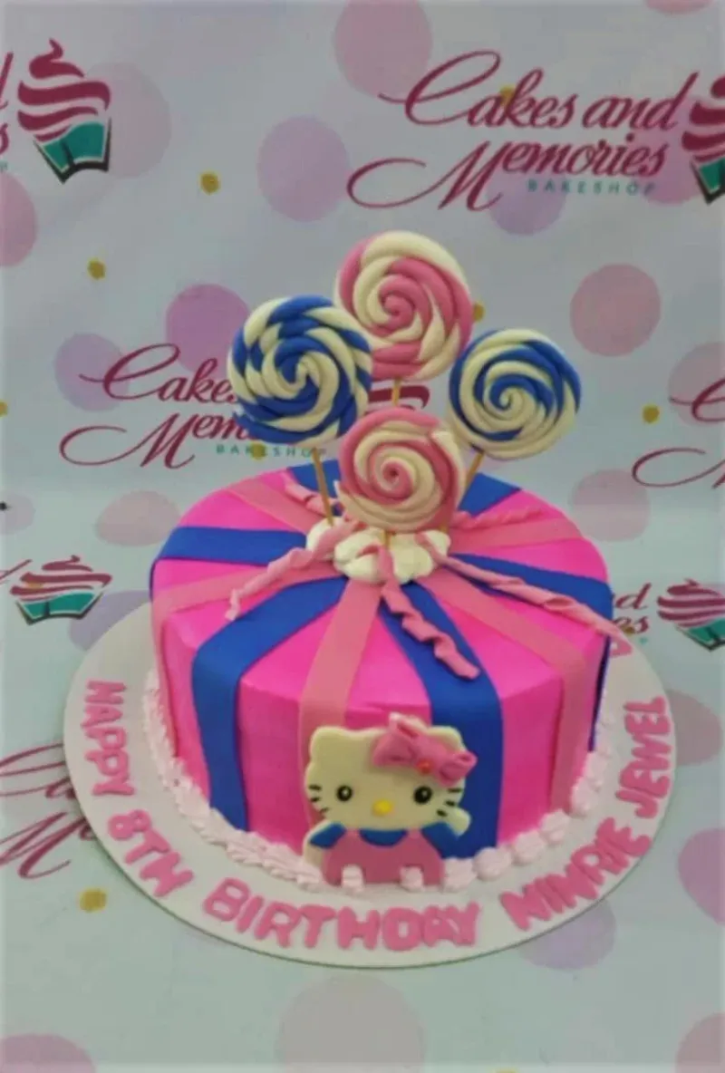 A pink and blue 1 Tier cake themed around Hello Kitty, featuring a Hello Kitty character, swirl lollipop toppers, and pink icing borders. A pink and blue 1 Tier cake themed around Hello Kitty, featuring a Hello Kitty character, swirl lollipop toppers, and pink icing borders.