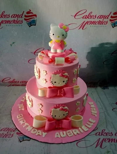 A pink two-tier fondant cake themed around Hello Kitty, featuring a 3D Hello Kitty figure and fondant bows with a personalized message. A pink two-tier fondant cake themed around Hello Kitty, featuring a 3D Hello Kitty figure and fondant bows with a personalized message.