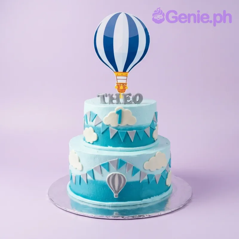 A light blue two-tier Hot Air Balloon cake featuring a large blue and white striped balloon topper, white clouds, and blue bunting. A light blue two-tier Hot Air Balloon cake featuring a large blue and white striped balloon topper, white clouds, and blue bunting.