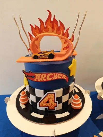 Blue 2-tier birthday cake with smooth blue icing, a Hot Wheels flame topper, and a gold toy race car Blue 2-tier birthday cake with smooth blue icing, a Hot Wheels flame topper, and a gold toy race car