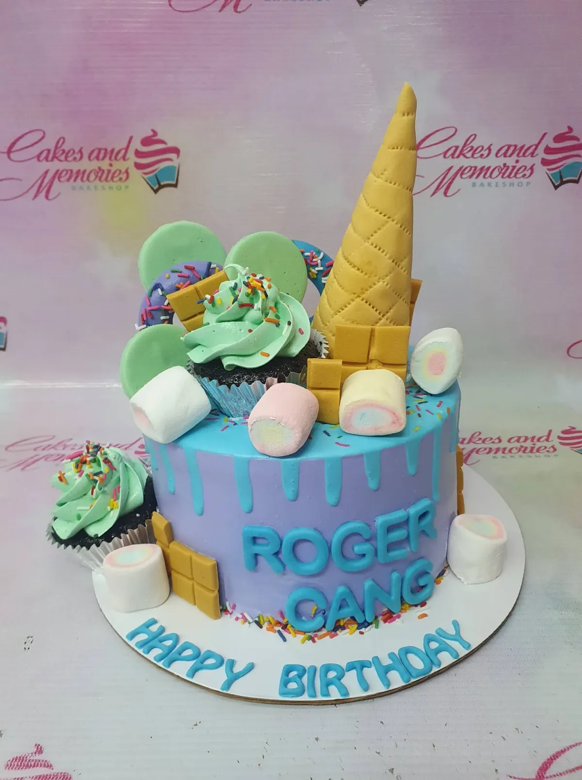 Purple and blue birthday cake with an ice cream cone topper, chocolate bars, marshmallows, and cupcakes. Purple and blue birthday cake with an ice cream cone topper, chocolate bars, marshmallows, and cupcakes.