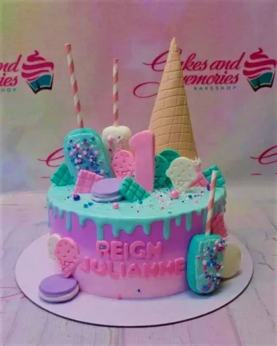 A pink and blue 1-tier cake themed around ice cream, featuring a large waffle cone, popsicles, and macarons. A pink and blue 1-tier cake themed around ice cream, featuring a large waffle cone, popsicles, and macarons.