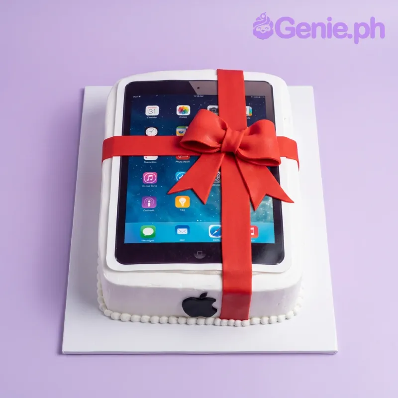 White rectangular cake designed to look like an iPad with a large red fondant bow and a printed screen showing app icons. White rectangular cake designed to look like an iPad with a large red fondant bow and a printed screen showing app icons.