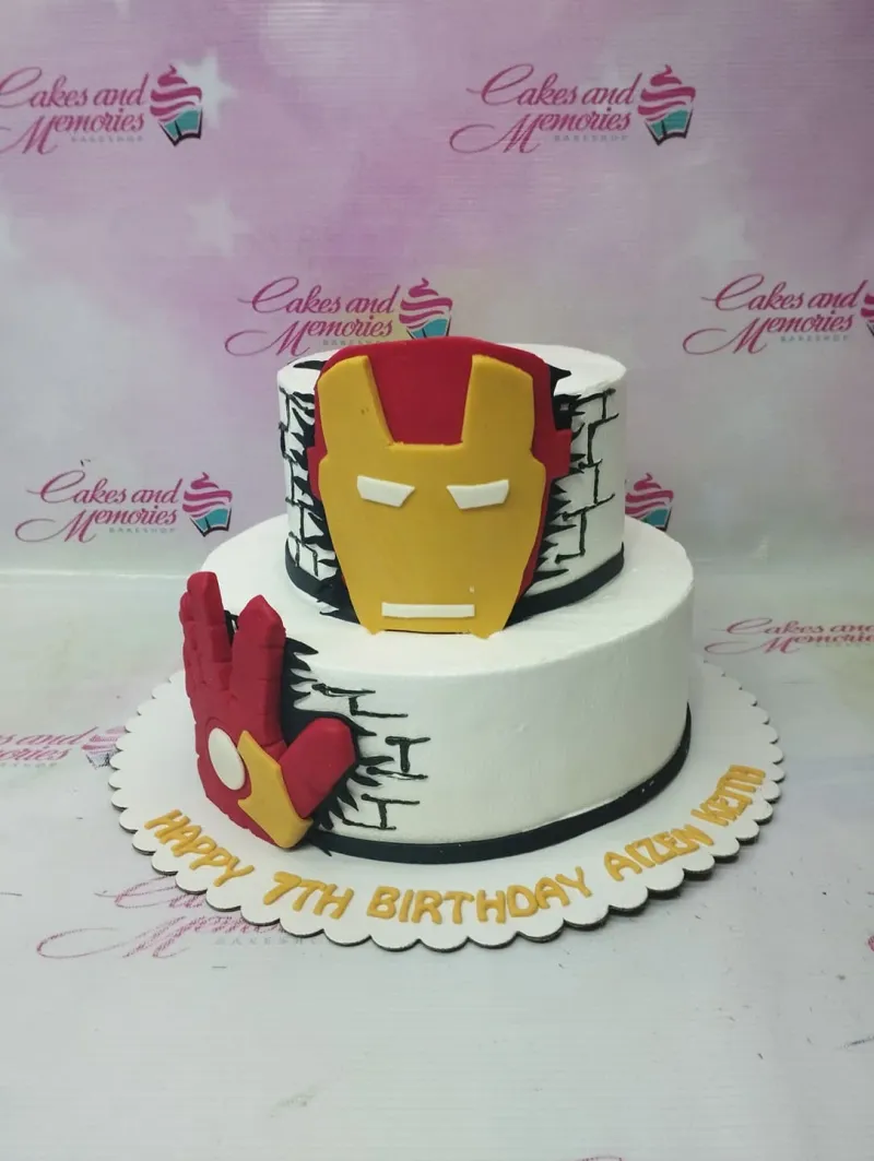 Iron Man themed 2-tier white cake with red and yellow fondant mask and hand toppers and black brick wall icing details. Iron Man themed 2-tier white cake with red and yellow fondant mask and hand toppers and black brick wall icing details.