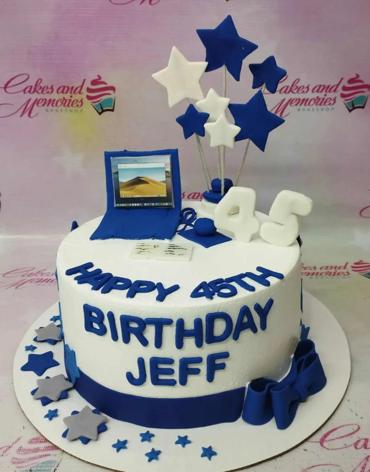 A white and blue 1-tier IT Professional cake, featuring a blue laptop, white number 45, and blue and white stars. A white and blue 1-tier IT Professional cake, featuring a blue laptop, white number 45, and blue and white stars.