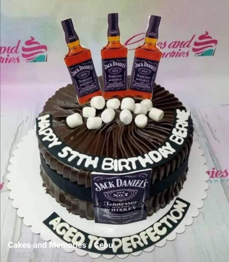 A brown, black, and white 1-tier cake themed around Jack Daniels, featuring bottle printouts, marshmallows, and a black fondant band with text. A brown, black, and white 1-tier cake themed around Jack Daniels, featuring bottle printouts, marshmallows, and a black fondant band with text.