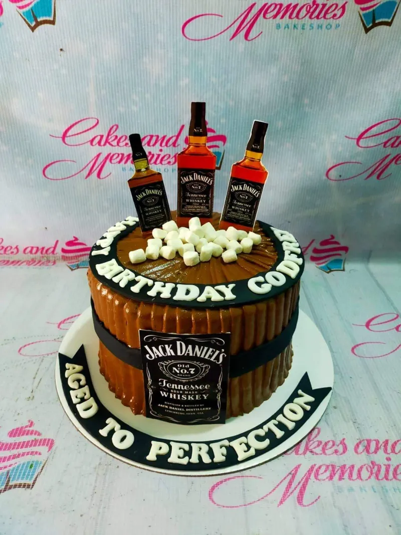 A brown barrel-style 1-Tier cake themed around Jack Daniels, featuring whiskey bottle printouts, a brand label, white marshmallows, and custom text. A brown barrel-style 1-Tier cake themed around Jack Daniels, featuring whiskey bottle printouts, a brand label, white marshmallows, and custom text.