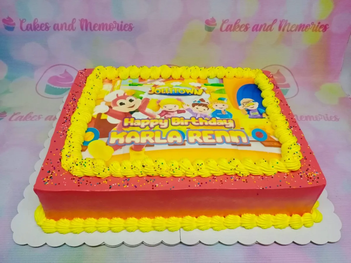 A red-orange rectangle cake themed Jollitown, featuring a Jollitown character printout, yellow piped borders, and sprinkles. A red-orange rectangle cake themed Jollitown, featuring a Jollitown character printout, yellow piped borders, and sprinkles.
