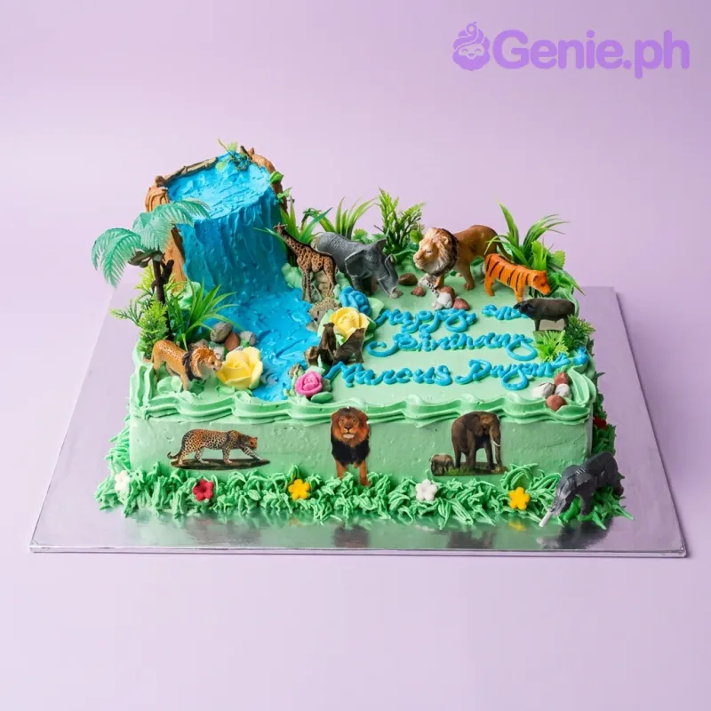 A green and blue rectangle Jungle Safari cake, with plastic animal toys, a blue icing waterfall, and green grass borders. A green and blue rectangle Jungle Safari cake, with plastic animal toys, a blue icing waterfall, and green grass borders.
