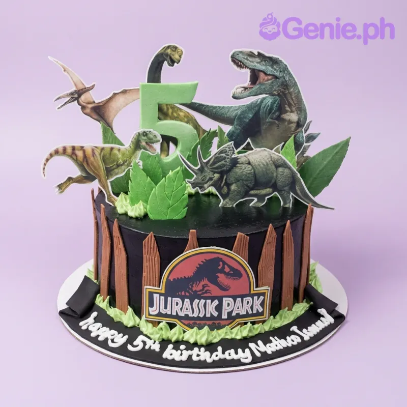 A black and green 1 Tier cake themed around Jurassic Park, featuring a green number 5, dinosaur and logo printouts, and green fondant leaves. A black and green 1 Tier cake themed around Jurassic Park, featuring a green number 5, dinosaur and logo printouts, and green fondant leaves.