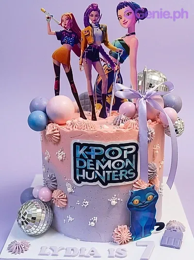 A purple and pink gradient 1-tier K-Pop Demon Hunters cake, featuring character and logo printouts, silver disco balls, and a lavender satin ribbon. A purple and pink gradient 1-tier K-Pop Demon Hunters cake, featuring character and logo printouts, silver disco balls, and a lavender satin ribbon.