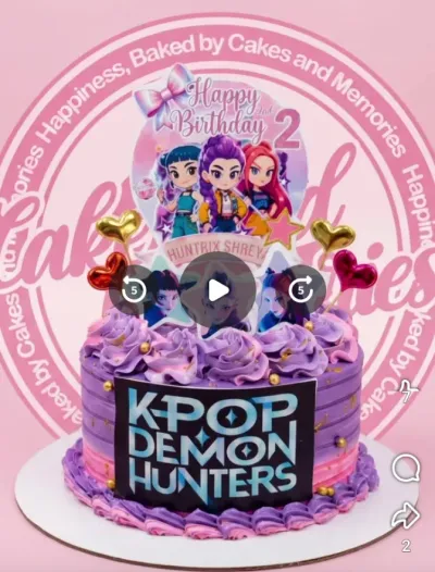 Purple and pink K-Pop Demon Hunters themed cake with character printouts, gold hearts, and piped icing rosettes. Purple and pink K-Pop Demon Hunters themed cake with character printouts, gold hearts, and piped icing rosettes.
