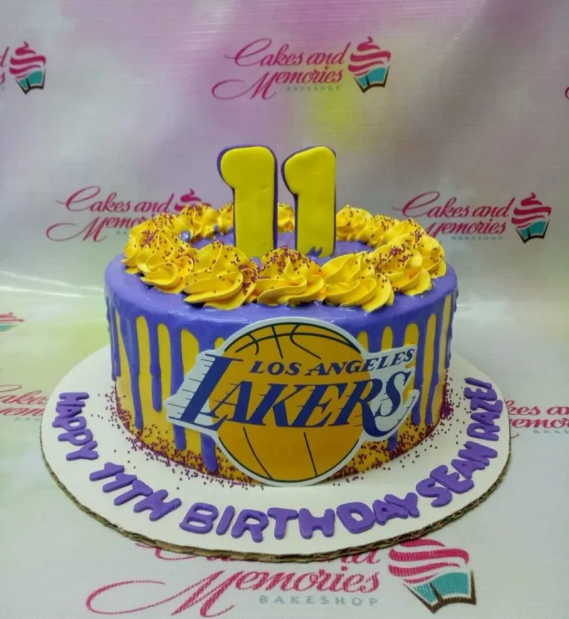 Purple Los Angeles Lakers themed birthday cake with yellow icing drips, yellow rosettes, and a large Lakers logo printout. Purple Los Angeles Lakers themed birthday cake with yellow icing drips, yellow rosettes, and a large Lakers logo printout.