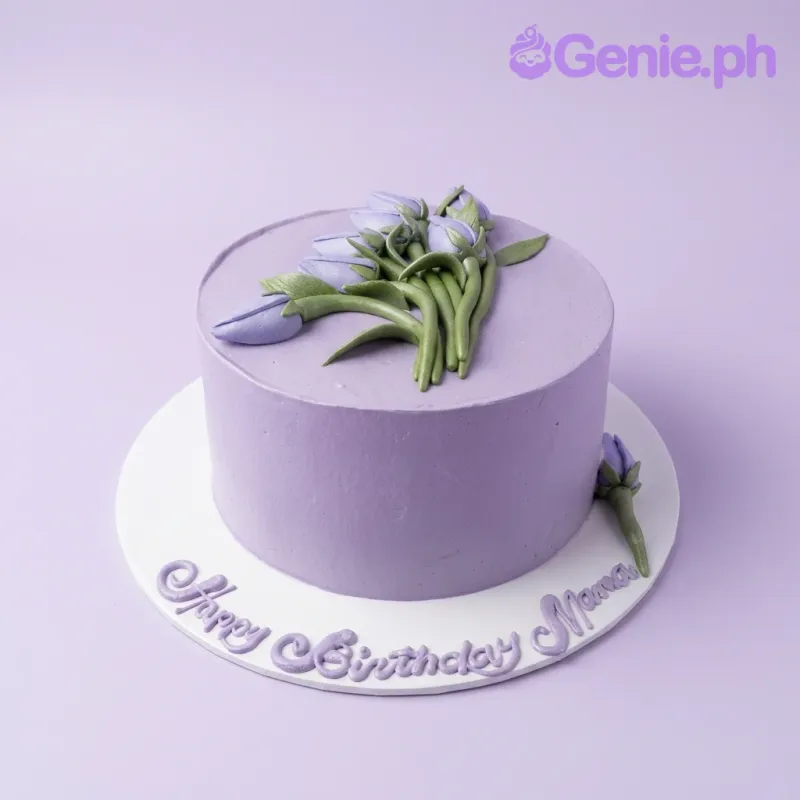 A lavender 1-tier cake with purple fondant tulip bouquet and green leaves, and text on base. A lavender 1-tier cake with purple fondant tulip bouquet and green leaves, and text on base.