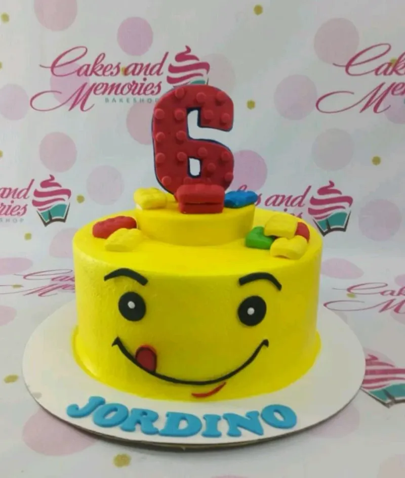 A yellow 1-tier Lego Head cake with a large red number 6 topper and colorful fondant building blocks. A yellow 1-tier Lego Head cake with a large red number 6 topper and colorful fondant building blocks.