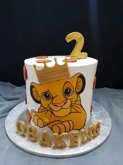 White 1-tier birthday cake with smooth soft icing, Simba theme, and a gold crown with paw prints White 1-tier birthday cake with smooth soft icing, Simba theme, and a gold crown with paw prints