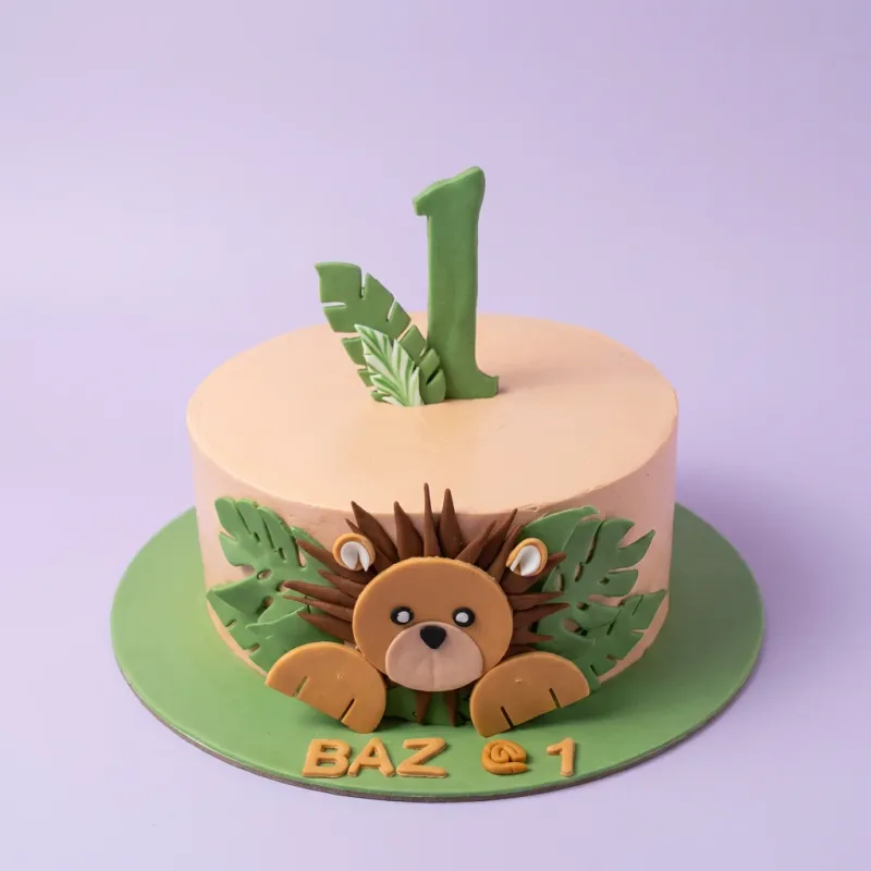 A peach and green 1 Tier cake themed around Lion Safari, featuring a 3D lion face and a green number one, with fondant leaves. A peach and green 1 Tier cake themed around Lion Safari, featuring a 3D lion face and a green number one, with fondant leaves.