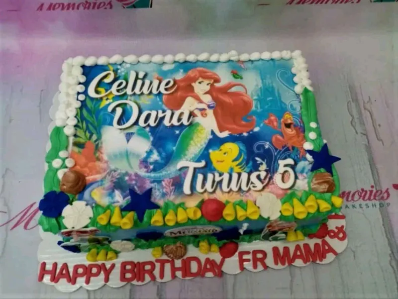A blue and white Rectangle Little Mermaid cake with an Ariel printout, white icing borders, colorful gumpaste sea decorations, and edible text. A blue and white Rectangle Little Mermaid cake with an Ariel printout, white icing borders, colorful gumpaste sea decorations, and edible text.