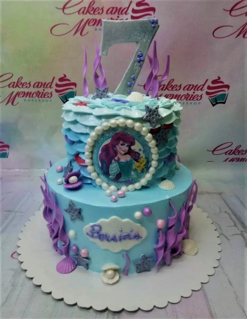 A light blue two-tier Little Mermaid cake with a silver 7 topper, Ariel portrait, purple seaweed, and silver stars. A light blue two-tier Little Mermaid cake with a silver 7 topper, Ariel portrait, purple seaweed, and silver stars.