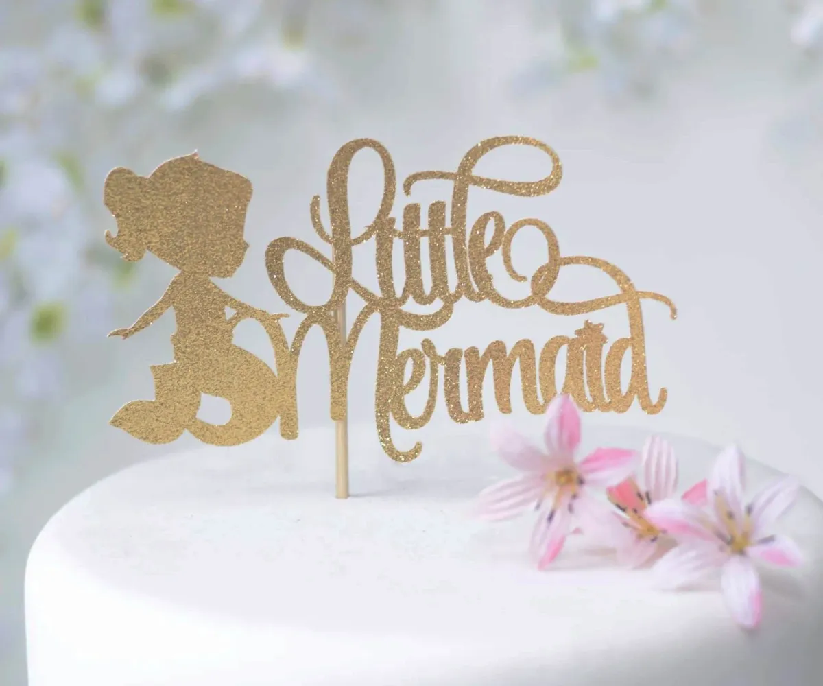 A white 1 Tier Fondant cake themed around Little Mermaid, featuring a gold glitter mermaid topper and pink and white flowers. A white 1 Tier Fondant cake themed around Little Mermaid, featuring a gold glitter mermaid topper and pink and white flowers.
