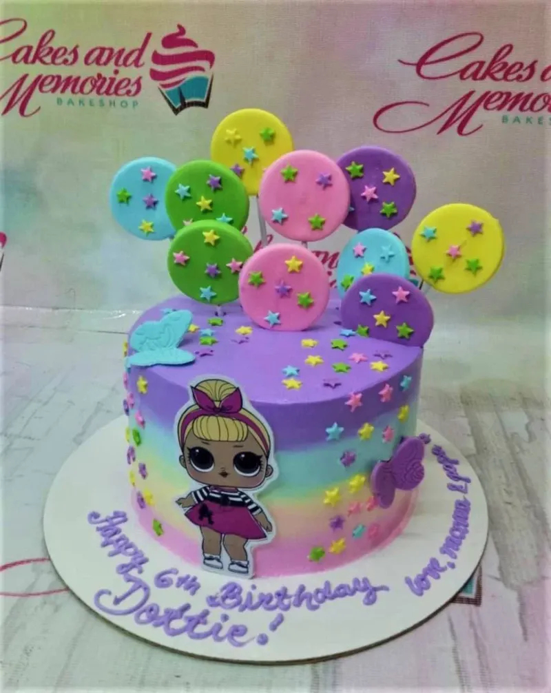 A rainbow 1-tier cake themed around LOL Surprise, featuring a character printout and star lollipops. A rainbow 1-tier cake themed around LOL Surprise, featuring a character printout and star lollipops.