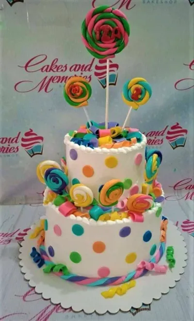 Colorful 2-tier lollipop themed birthday cake with white icing, multi-colored polka dots, and fondant lollipop toppers. Colorful 2-tier lollipop themed birthday cake with white icing, multi-colored polka dots, and fondant lollipop toppers.