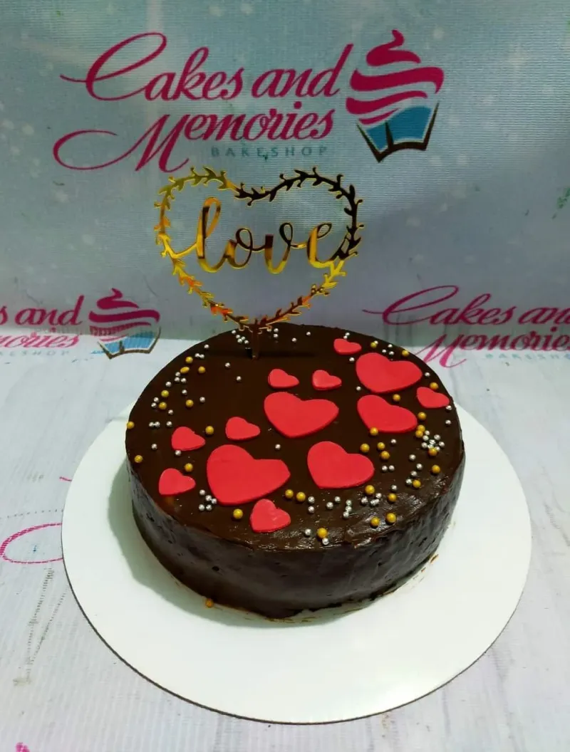 A dark brown 1-tier cake themed Love Heart, with a gold 'Love' heart topper, red fondant hearts, and gold and silver sprinkles. A dark brown 1-tier cake themed Love Heart, with a gold 'Love' heart topper, red fondant hearts, and gold and silver sprinkles.