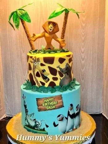 Soft yellow and teal 2-tier fondant cake with an Alex the lion figure, Madagascar character side panels, and green palm leaves Soft yellow and teal 2-tier fondant cake with an Alex the lion figure, Madagascar character side panels, and green palm leaves