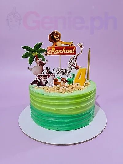 A green gradient 1-tier cake themed around Madagascar, featuring character printouts, a 'Ronhael' banner, and yellow candles. A green gradient 1-tier cake themed around Madagascar, featuring character printouts, a 'Ronhael' banner, and yellow candles.