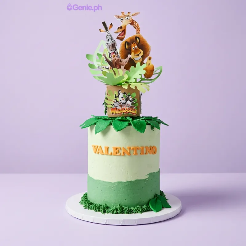 A green 1 Tier Madagascar themed cake, featuring character printouts, fondant leaves, and 'VALENTINO' text. A green 1 Tier Madagascar themed cake, featuring character printouts, fondant leaves, and 'VALENTINO' text.