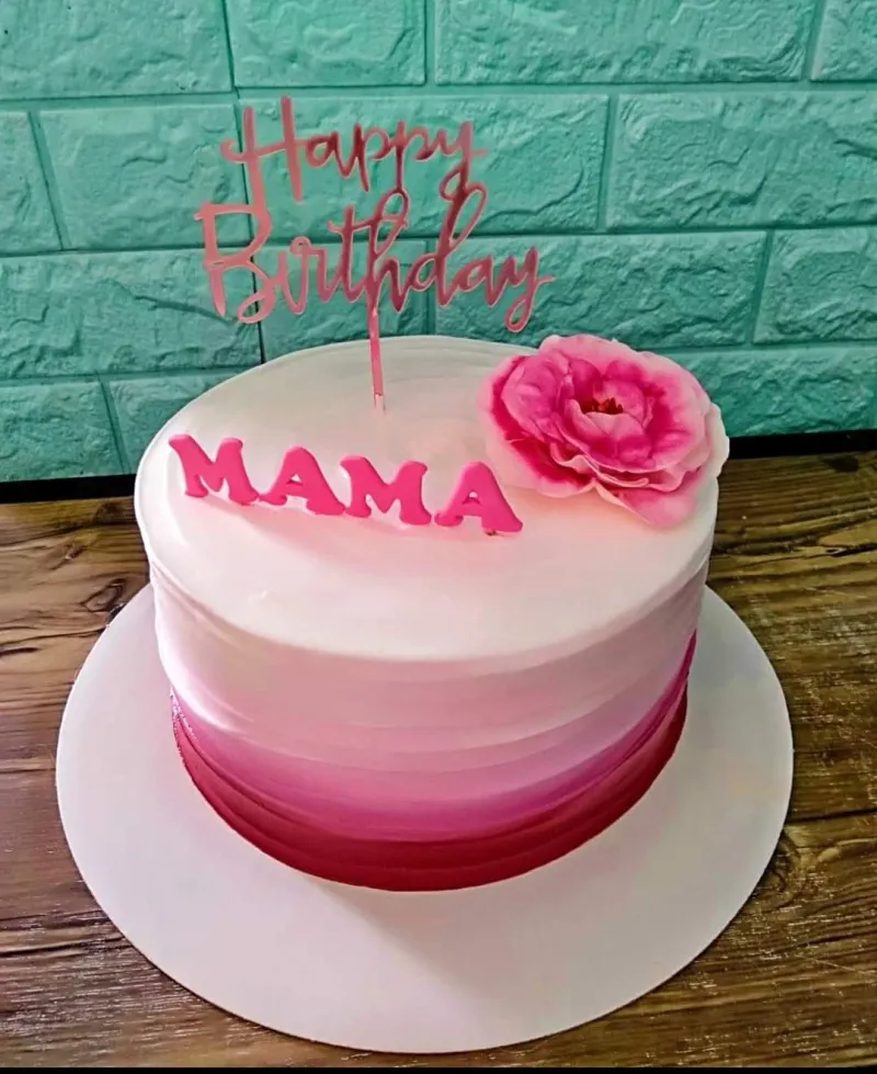 A pink and white 1-tier cake themed for Mama's birthday, featuring a pink 'Happy Birthday' topper, 'MAMA' letters, and a large pink edible flower. A pink and white 1-tier cake themed for Mama's birthday, featuring a pink 'Happy Birthday' topper, 'MAMA' letters, and a large pink edible flower.